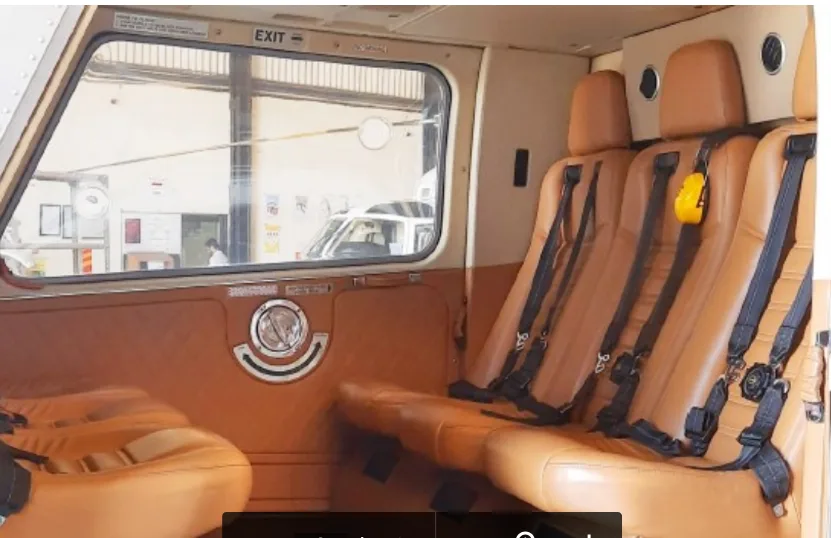 The interior of a helicopter cabin with tan leather seats and black seatbelts, looking towards the rear.