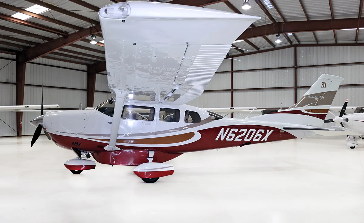 A side view of a white and red Cessna Stationair TC N6206X with its wing flaps extended, inside a hangar.