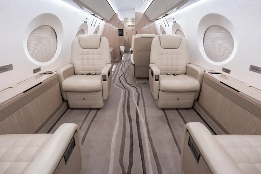 The luxurious interior cabin of a business jet, featuring light beige quilted leather seats and a patterned carpet.