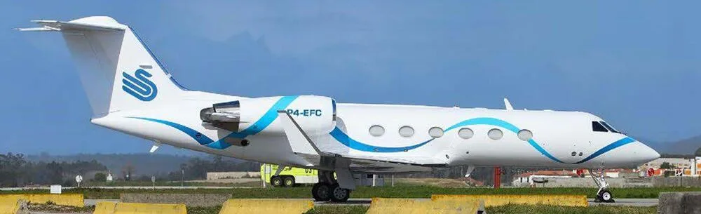 A Gulfstream G450 business jet with a white and blue wavy paint scheme parked on an airfield under a clear blue sky.