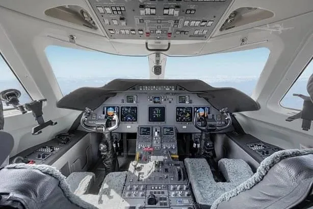 The modern cockpit of a business jet, featuring a glass panel display and dual yokes, with a clear view of the sky.