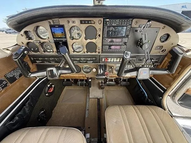 A detailed view of a small aircraft's cockpit, showing the instrument panel with analog gauges and digital screens, and dual control yokes.