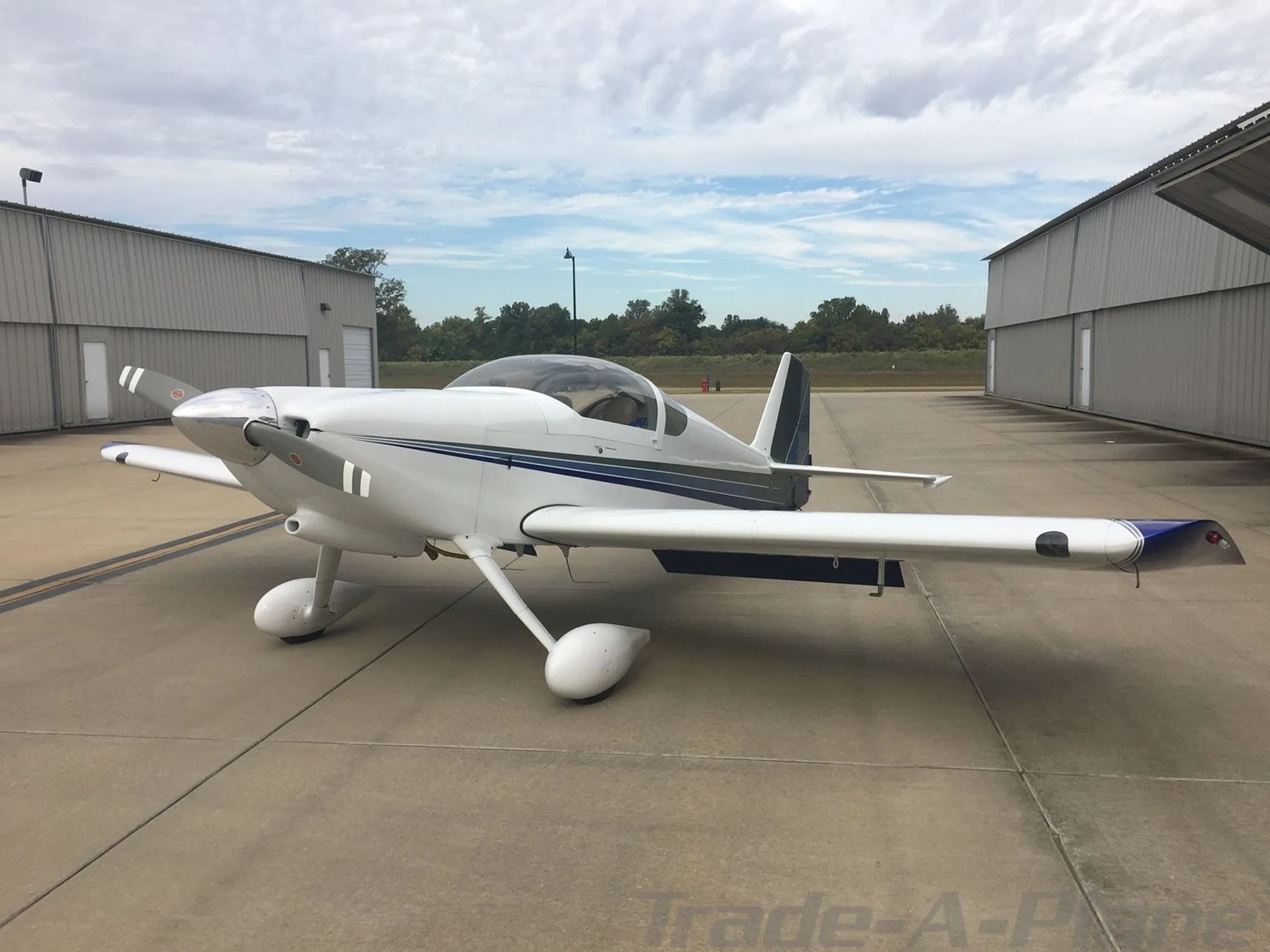 A front-side view of a white Van's RV-6 aircraft with blue and gray stripes parked on an airfield.