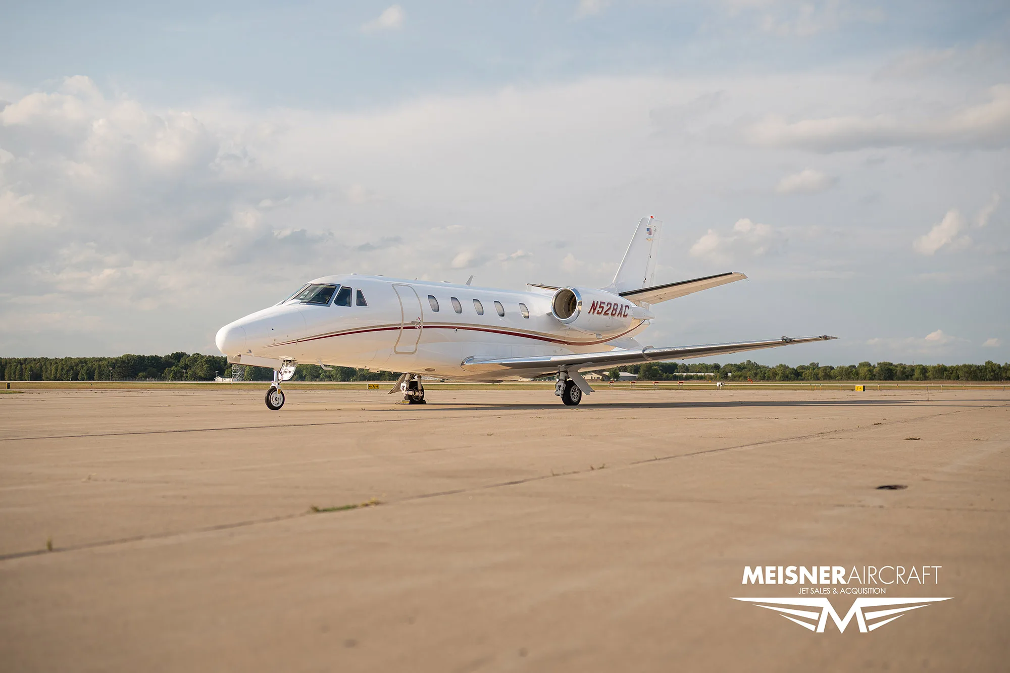 A white business jet with red stripes and registration N528AC parked on an airfield, with a 'Meisner Aircraft' logo.