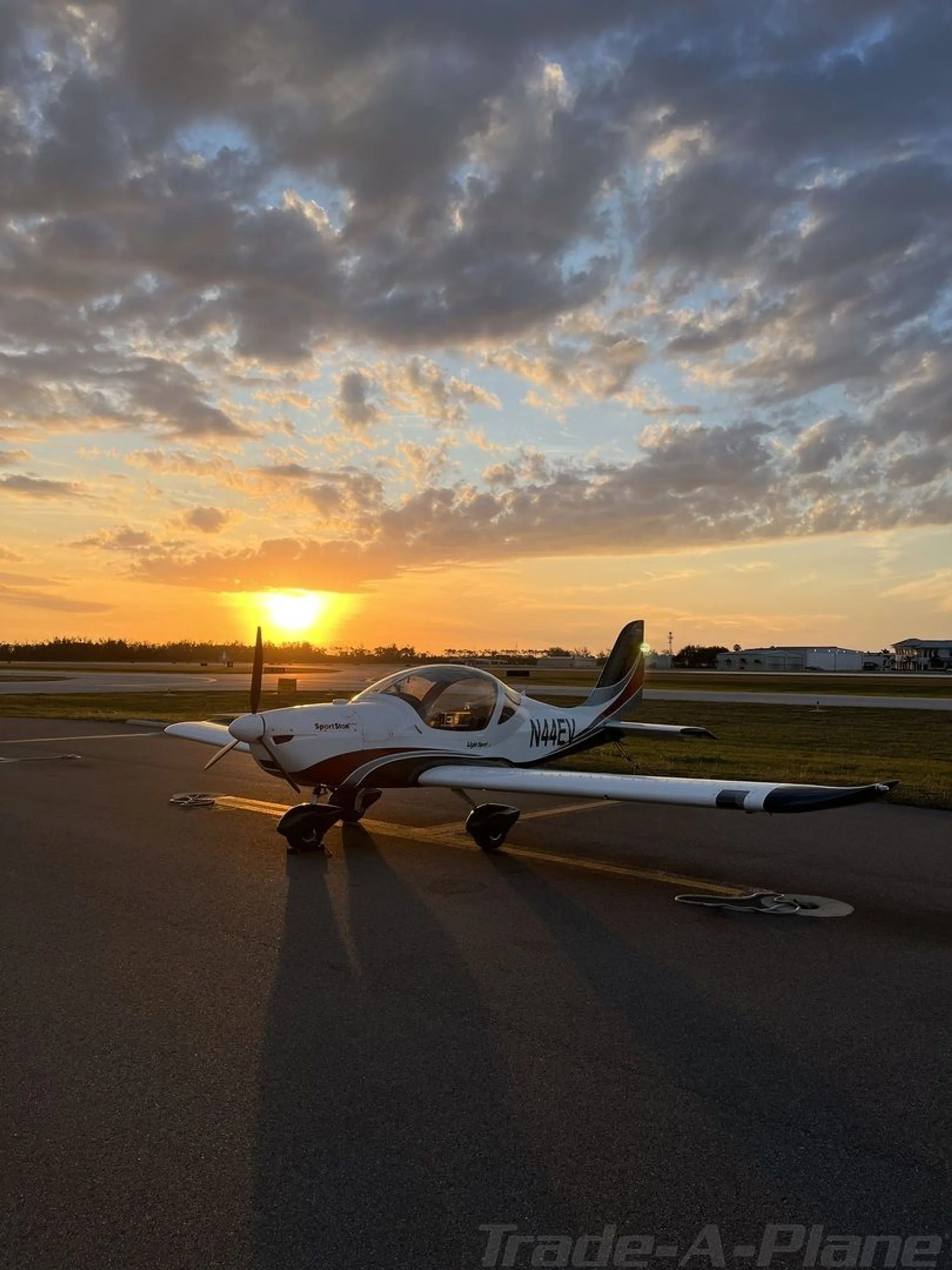 A white and red Evektor SportStar aircraft, tail number N44EV, is parked on an airfield at sunset.