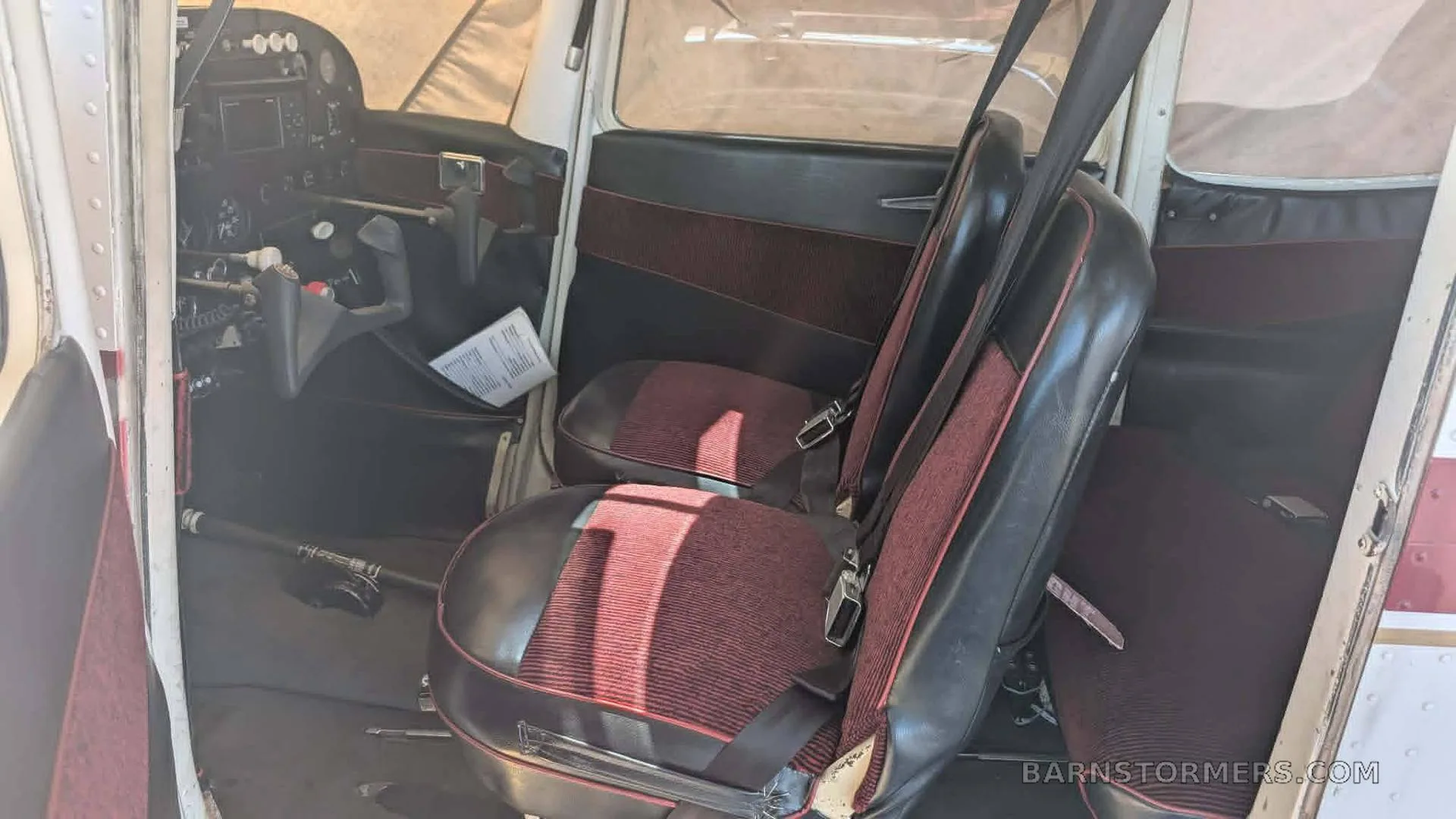 The interior of an aircraft showing the front seats with red striped fabric and a partial view of the instrument panel.
