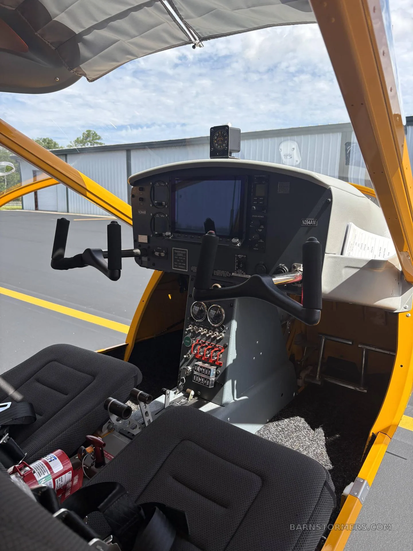 The cockpit of the yellow Aeroprakt A-32 Light Sport aircraft, showing the instrument panel, controls, and two black seats.