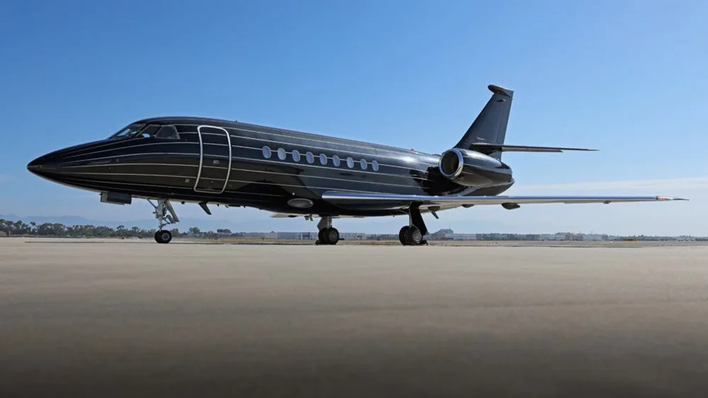 A sleek black business jet with white pinstripes is parked on a tarmac under a clear blue sky.