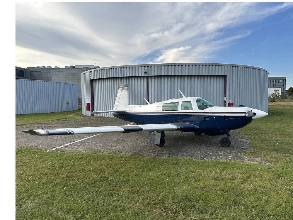 A blue and white single-engine aircraft parked on a tarmac next to a round hangar under a cloudy sky.