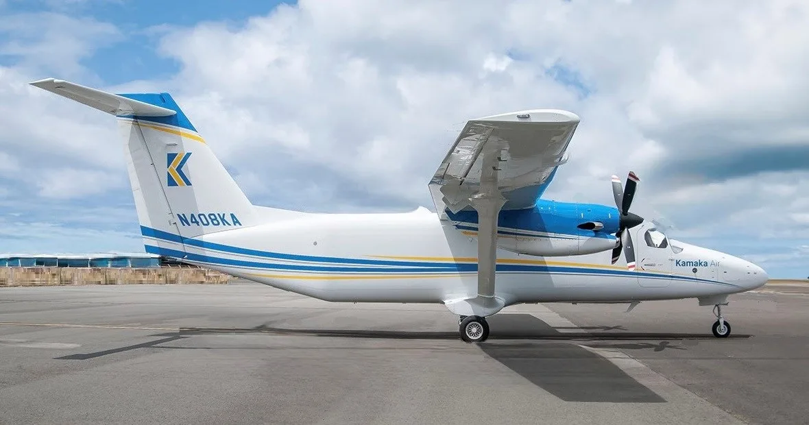 A white and blue Kamaka Air aircraft with tail number N408KA is parked on an airfield under a partly cloudy sky.