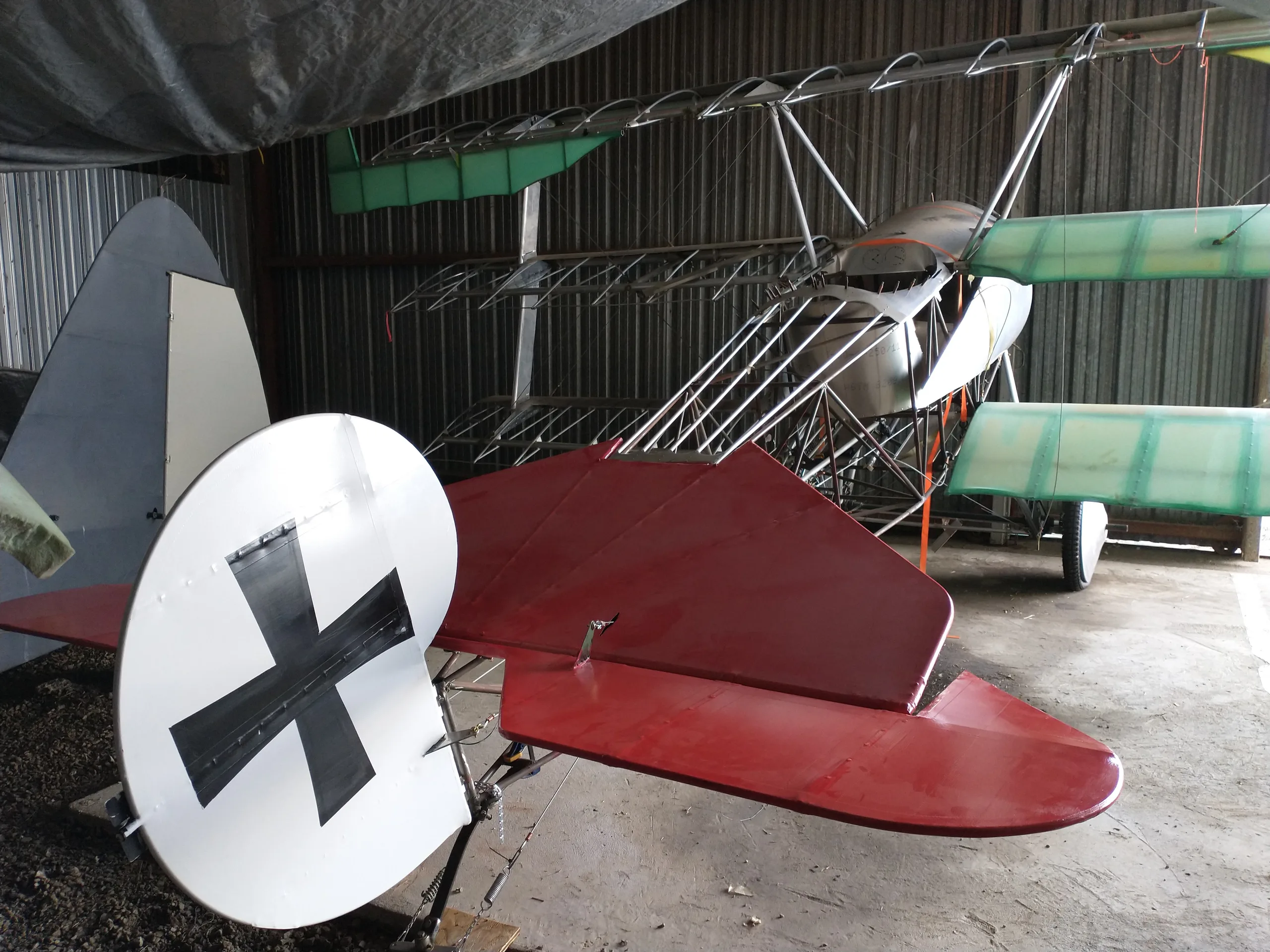 The red tail section of a triplane with a white roundel and black German cross insignia, stored inside a hangar.