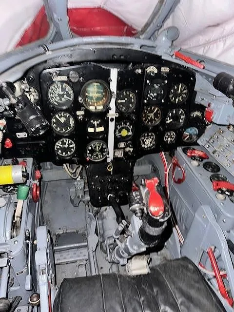 A wide view of a vintage jet aircraft cockpit, featuring the main instrument panel and various controls.