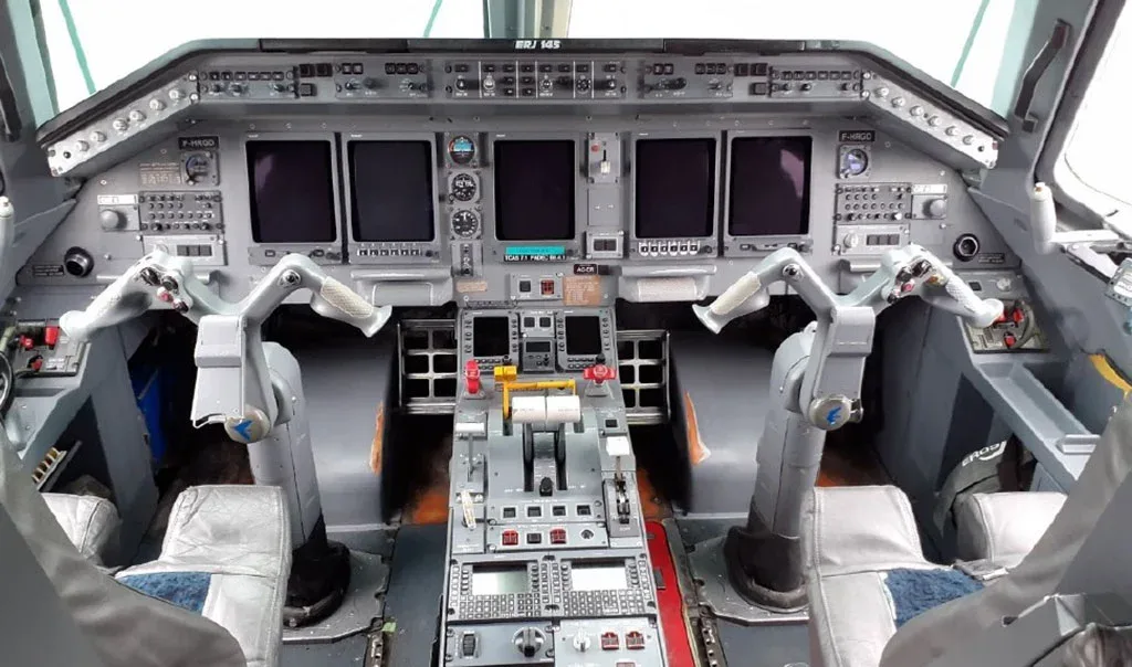 The cockpit of an Embraer ERJ-145 aircraft shows the instrument panel, multiple display screens, and control yokes.