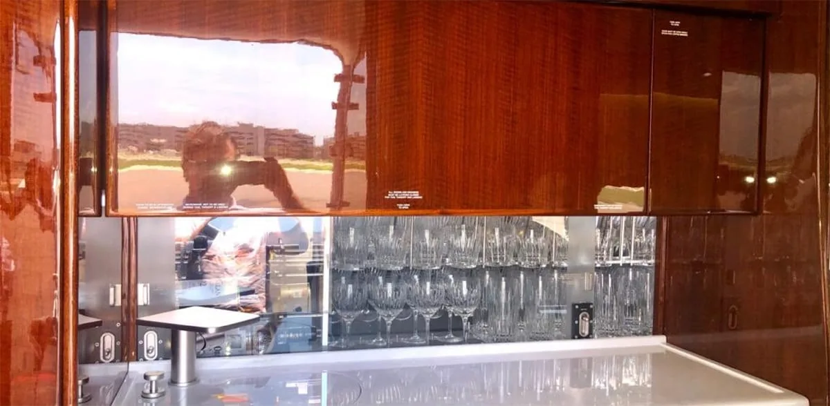 A close-up of the aircraft's galley with a counter, glassware, and reflective wood cabinetry.