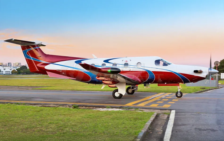 A white, red, and blue single-engine turboprop aircraft on an airport tarmac at dusk.