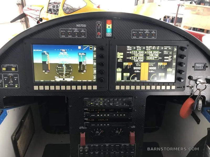 The cockpit instrument panel of a blue aircraft, featuring two large digital displays and various control switches.