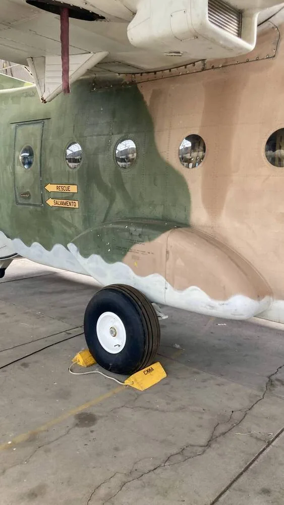 A close-up side view of a camouflage military transport aircraft's fuselage and landing gear.