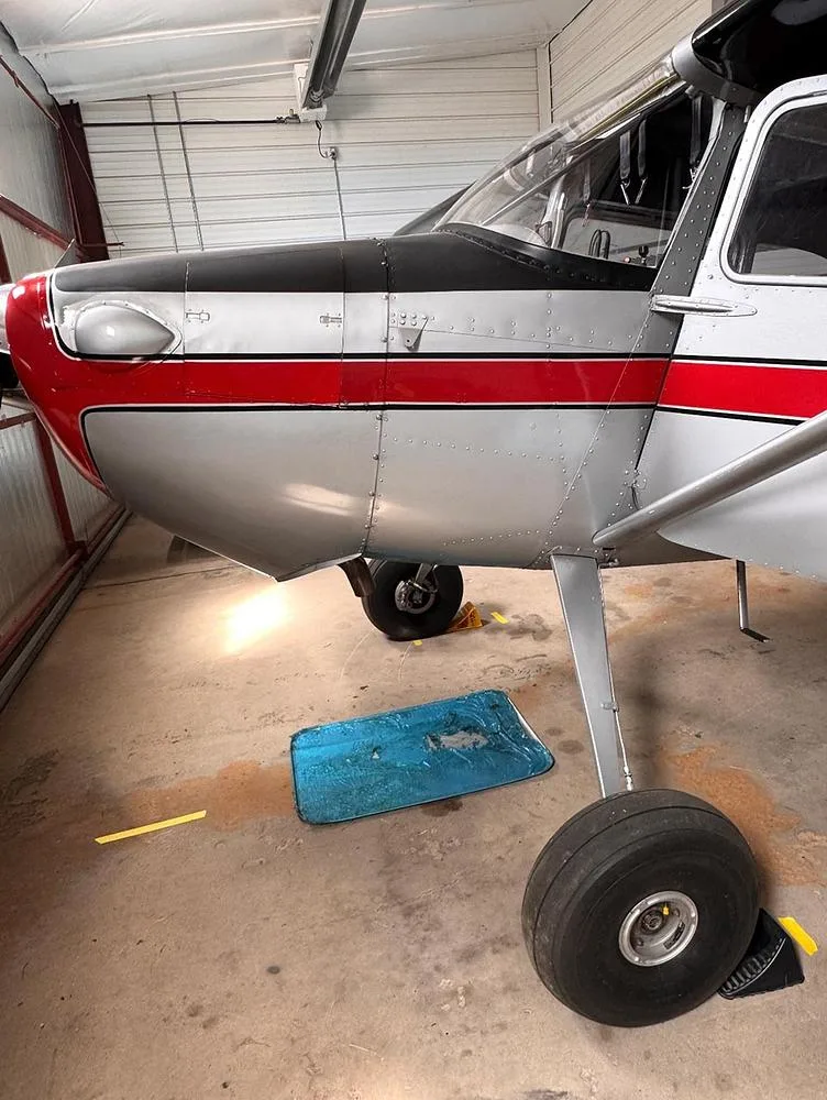 A close-up view of the front fuselage and main landing gear of a silver and red aircraft inside a hangar.