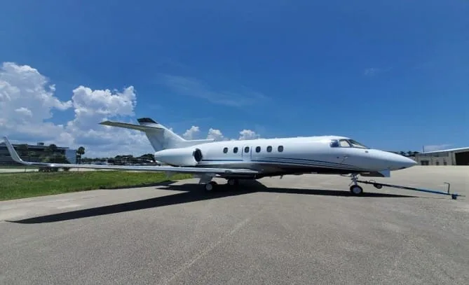 A white Cessna Citation X business jet parked on an asphalt tarmac under a blue sky with clouds.