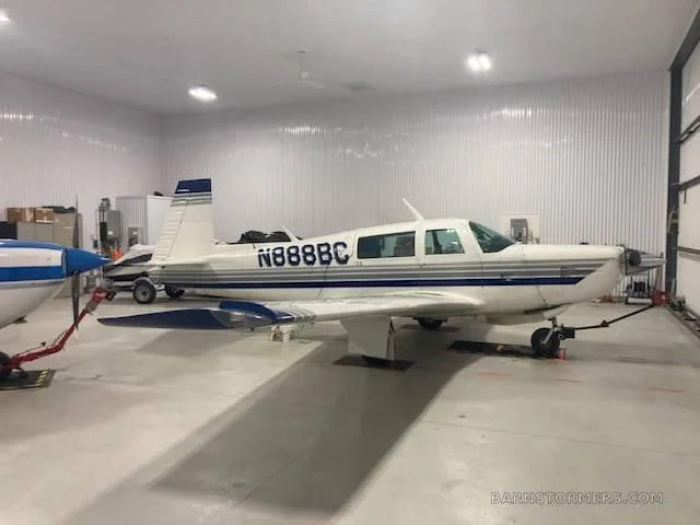 A white single-engine aircraft with blue and grey stripes (N888BC) parked inside a well-lit hangar.