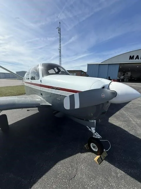 Front-side view of the N2194D Beechcraft Bonanza V-tail aircraft, parked on an airfield under a blue sky.