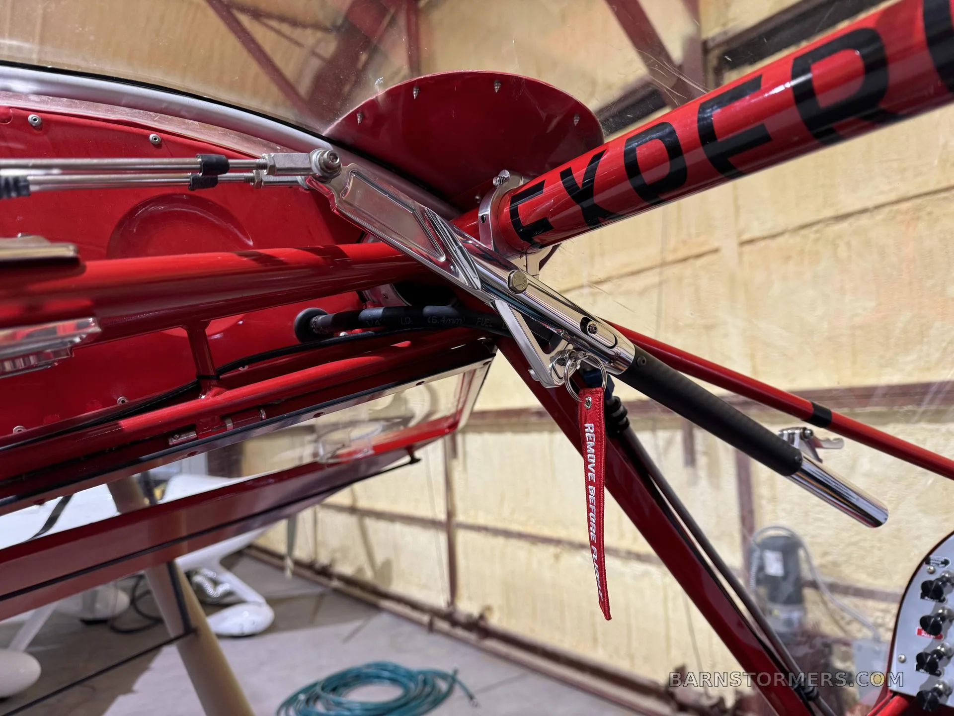 A close-up view of the red fuselage and wing strut attachment point of a light aircraft, with a "REMOVE BEFORE FLIGHT" tag.