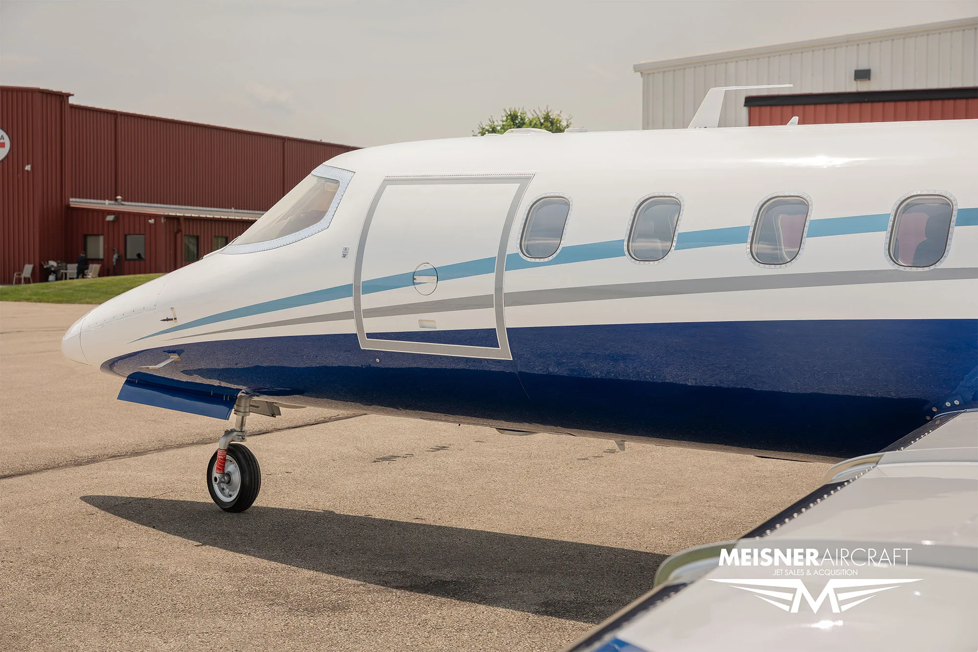 A close-up of the front fuselage of a white and blue Learjet, showing the cockpit and passenger door.