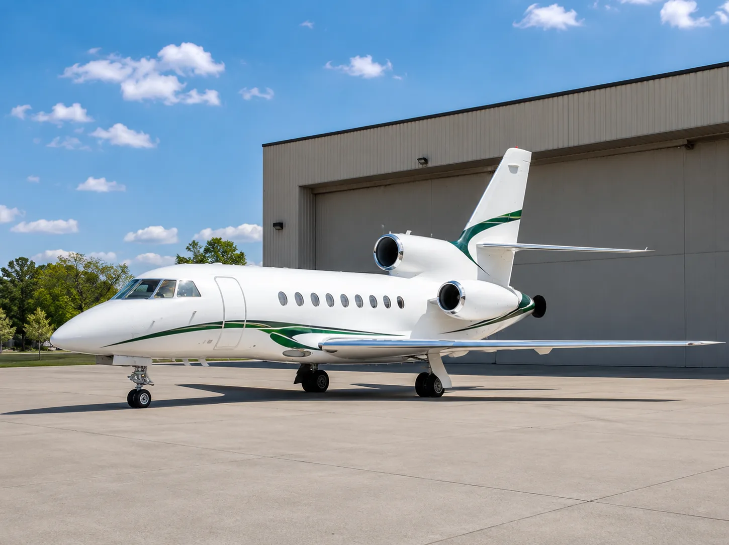 A white business jet with green stripes on the fuselage and tail, parked on a tarmac in front of a hangar under a blue sky.