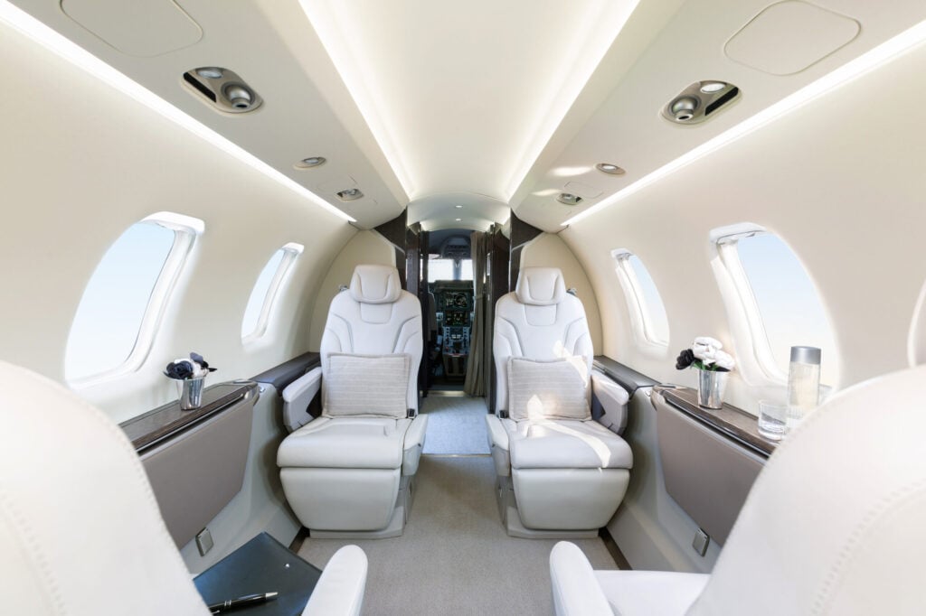 The interior of an aircraft cabin with white leather seats and light wood trim.