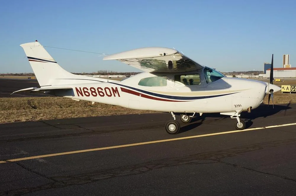 A white Cessna 210 Centurion aircraft with red, blue, and gold stripes parked on an airfield.