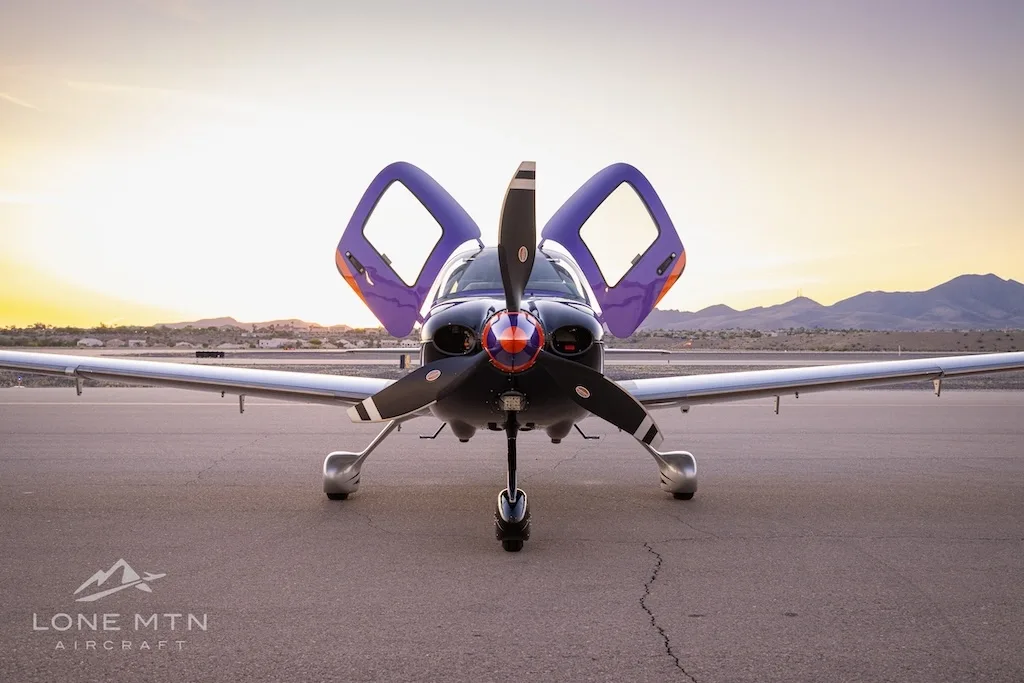 Front view of a purple and silver Cirrus SR22T with open doors, parked on a tarmac at sunset.