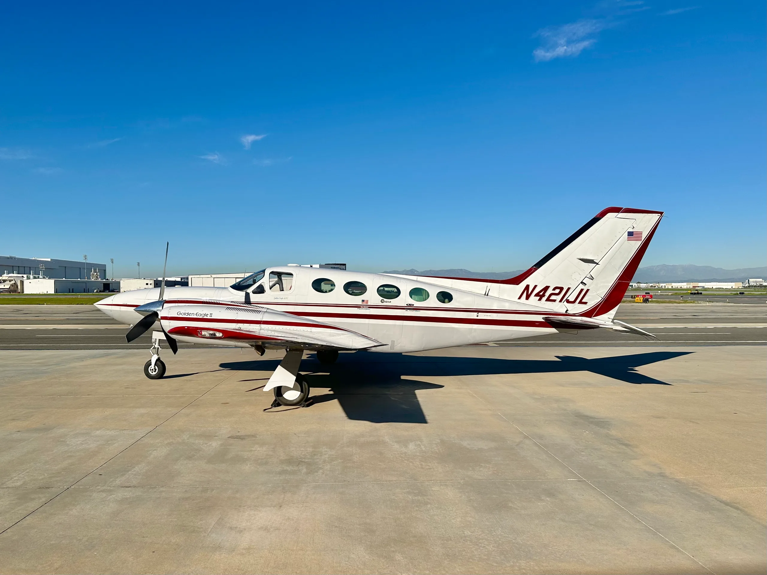A side view of a white and maroon Cessna 421 Golden Eagle II, registration N421JL, parked on an airfield.