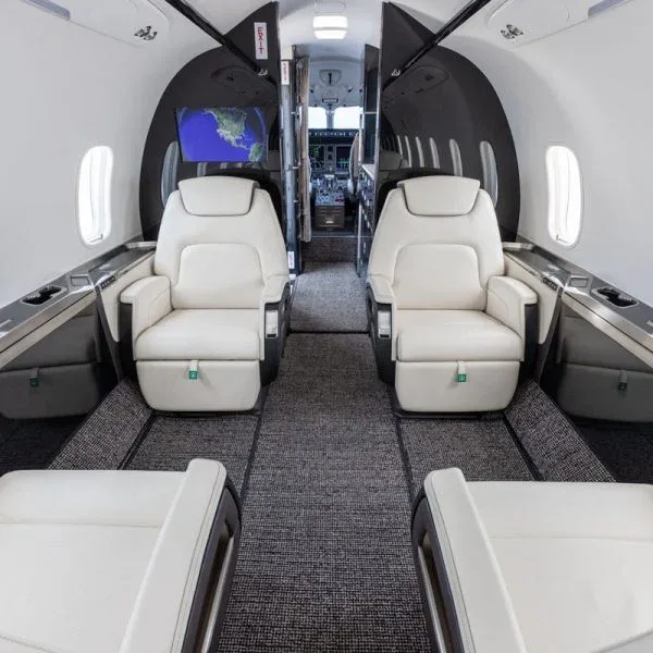 An interior view of a private jet cabin with cream leather seats, looking forward towards the cockpit.