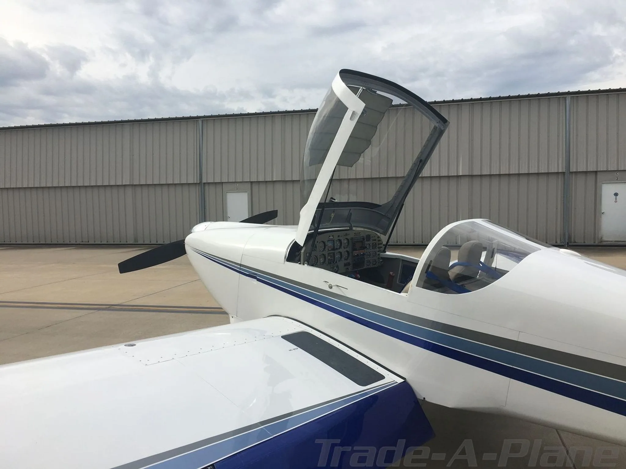 A close-up side view of a white Van's RV-6 aircraft with its canopy open, revealing the cockpit.