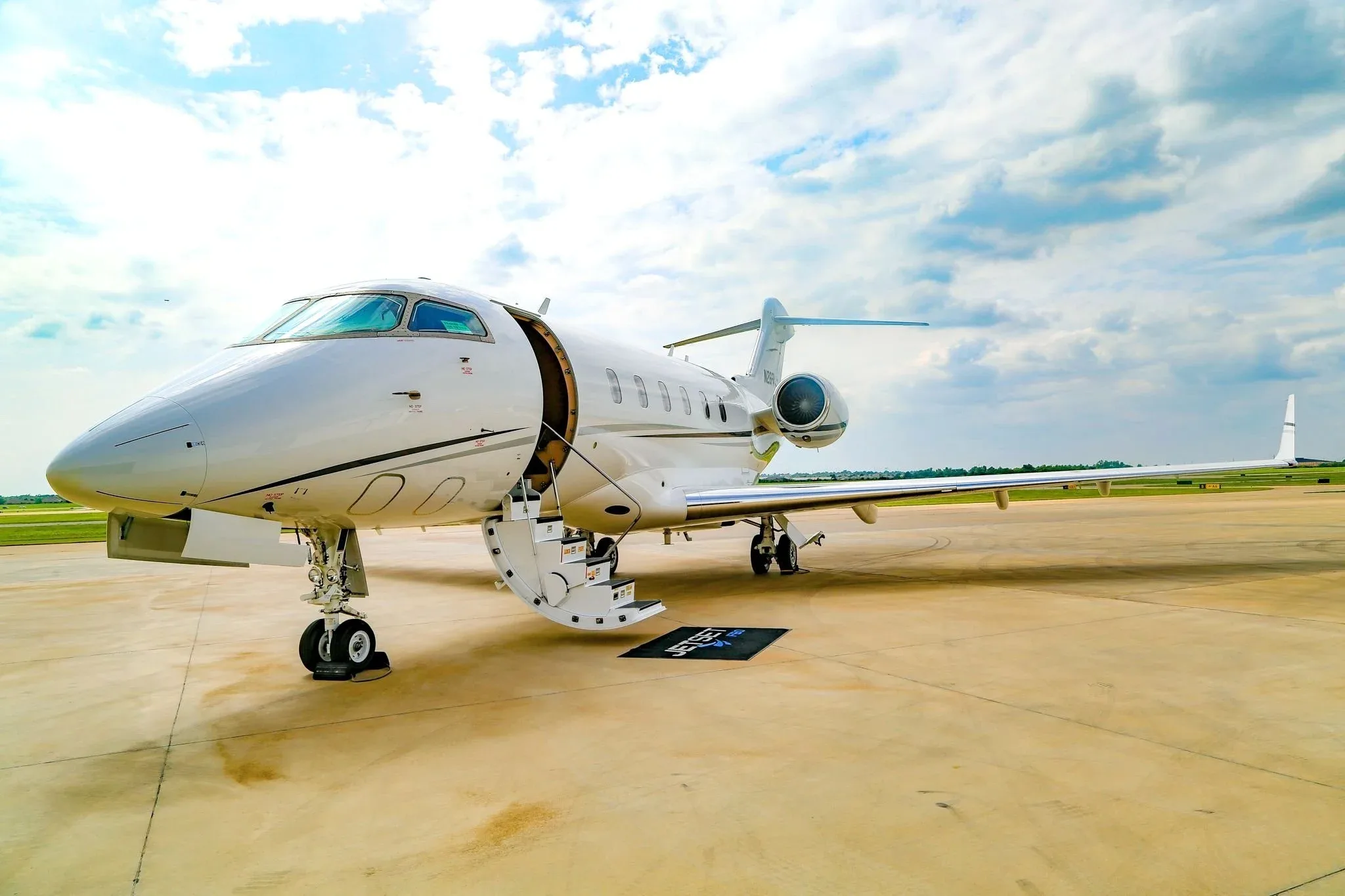 A white Bombardier Challenger 350 business jet, registration N26FA, is parked on a tarmac with its main door open and stairs extended, viewed from the front-right.