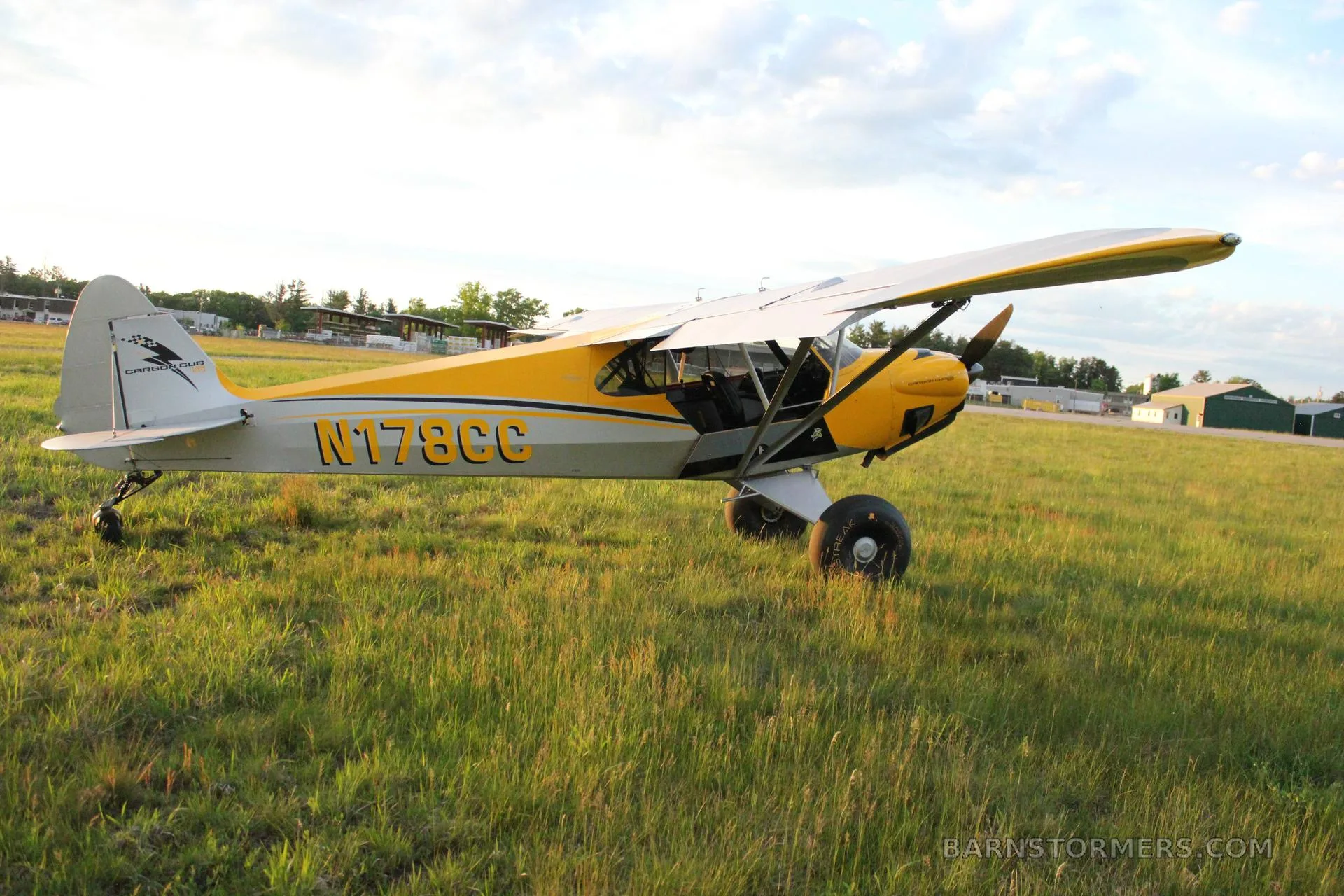 A yellow and grey Carbon Cub aircraft (N178CC) with large tires is parked on a grassy field.