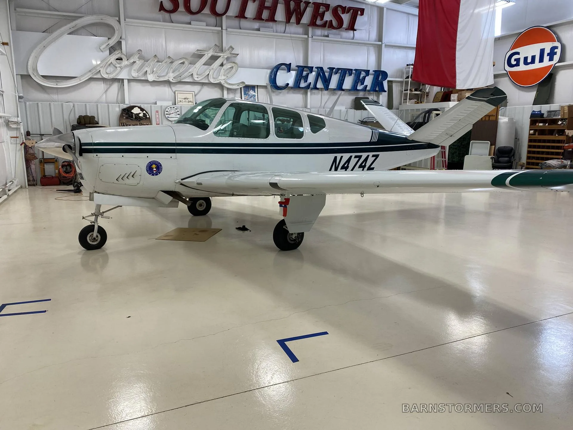 A white and dark green Beechcraft Bonanza with registration N474Z is parked in a hangar, viewed from the front-left.