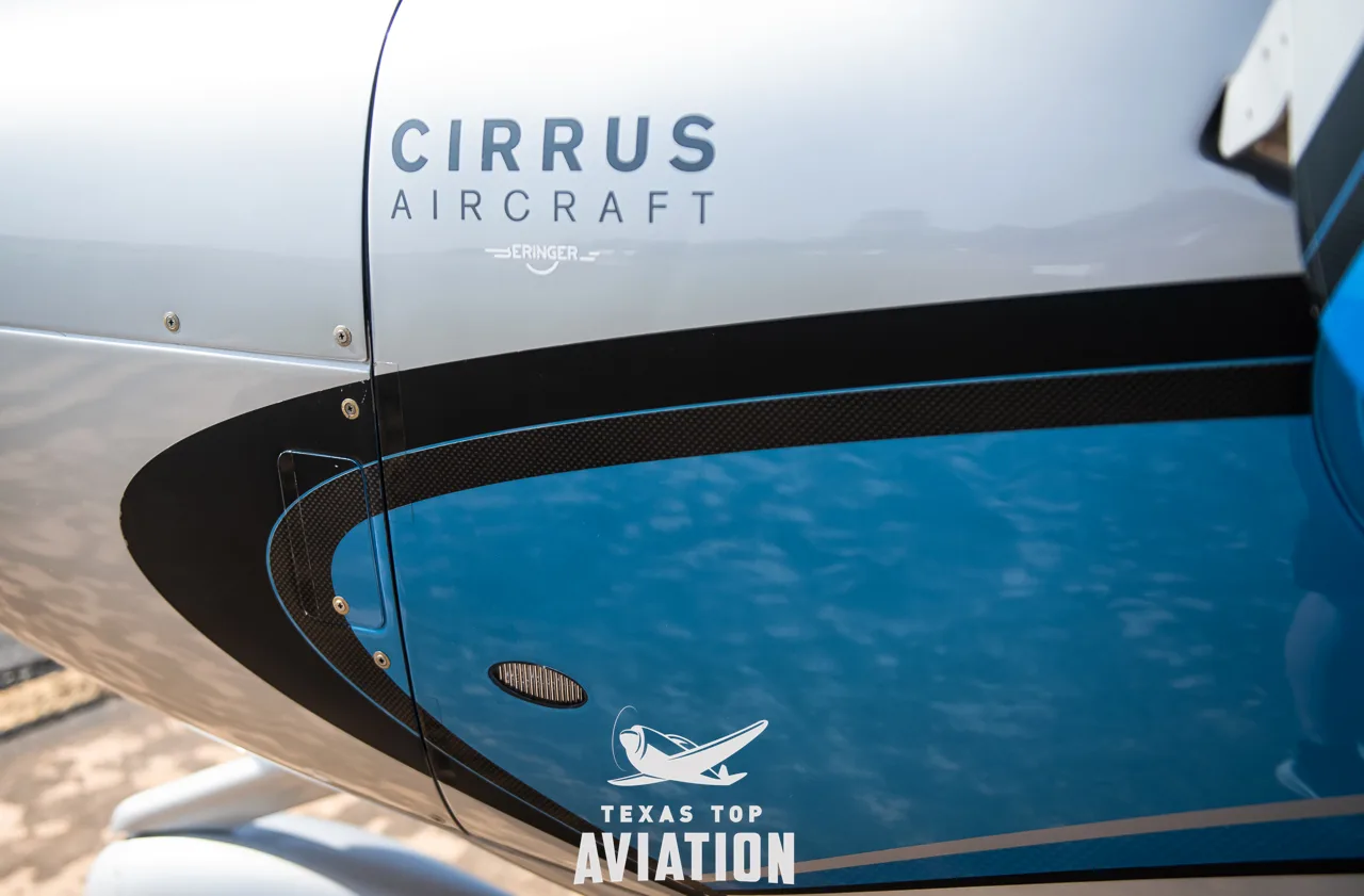 A close-up of the Cirrus SR22 aircraft's engine cowling, featuring "CIRRUS AIRCRAFT" text and blue and silver paint.