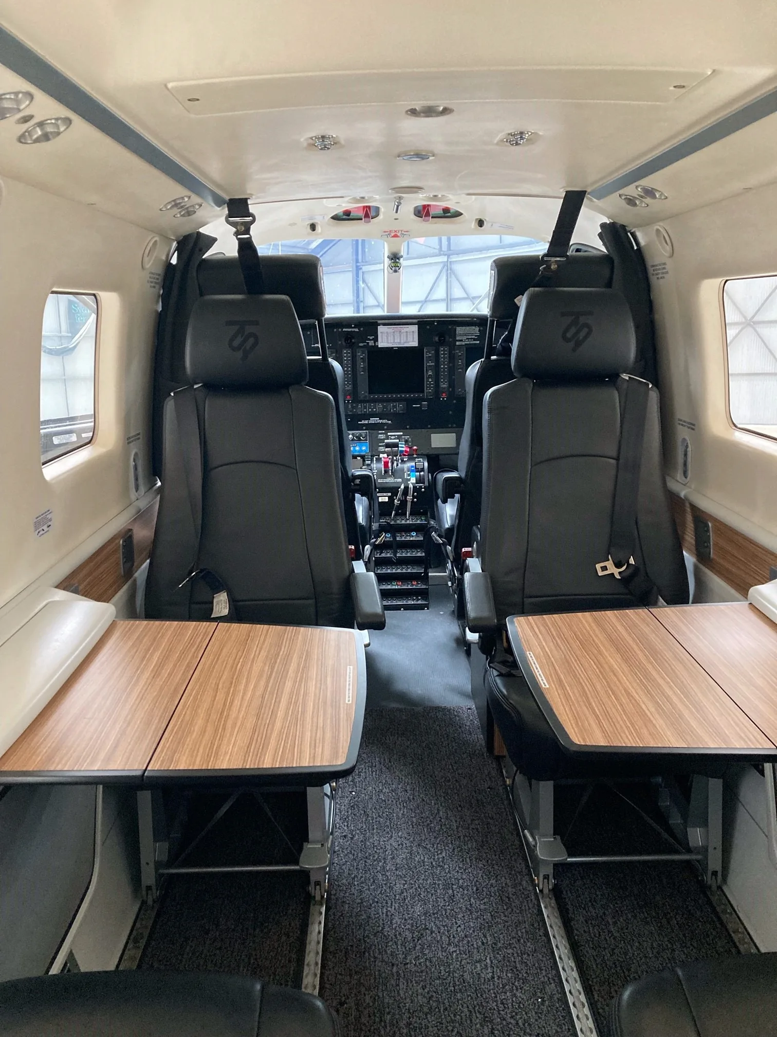 The interior cabin of a Quest Kodiak 100 aircraft, featuring black leather seats with fold-out wooden tables.