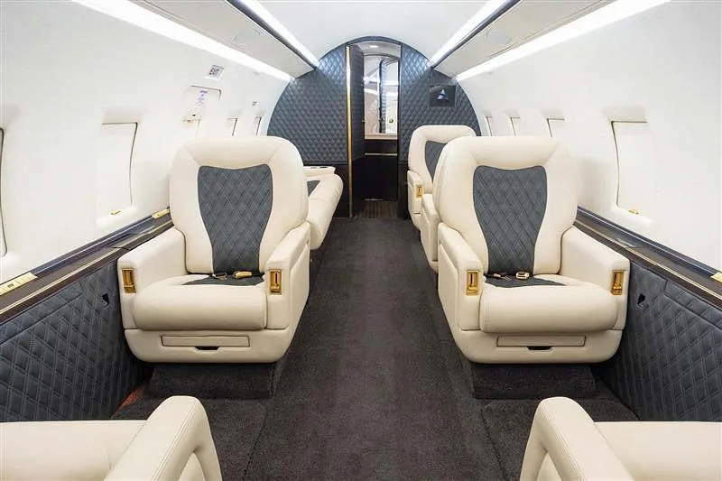 The luxurious interior cabin of a business jet, featuring cream and dark grey quilted leather seats.