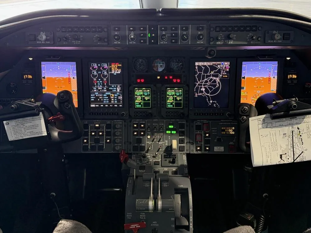The cockpit of a private jet with multiple digital displays, control yokes, and a throttle quadrant.