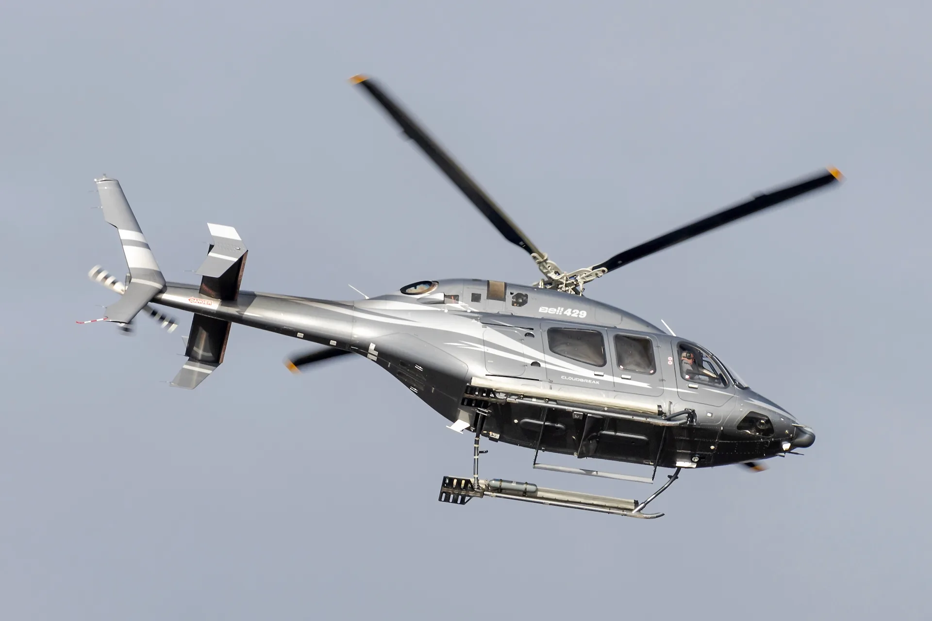 A grey Bell 429 helicopter with white accents and 'CLOUD BREAK' text flies against a clear sky.