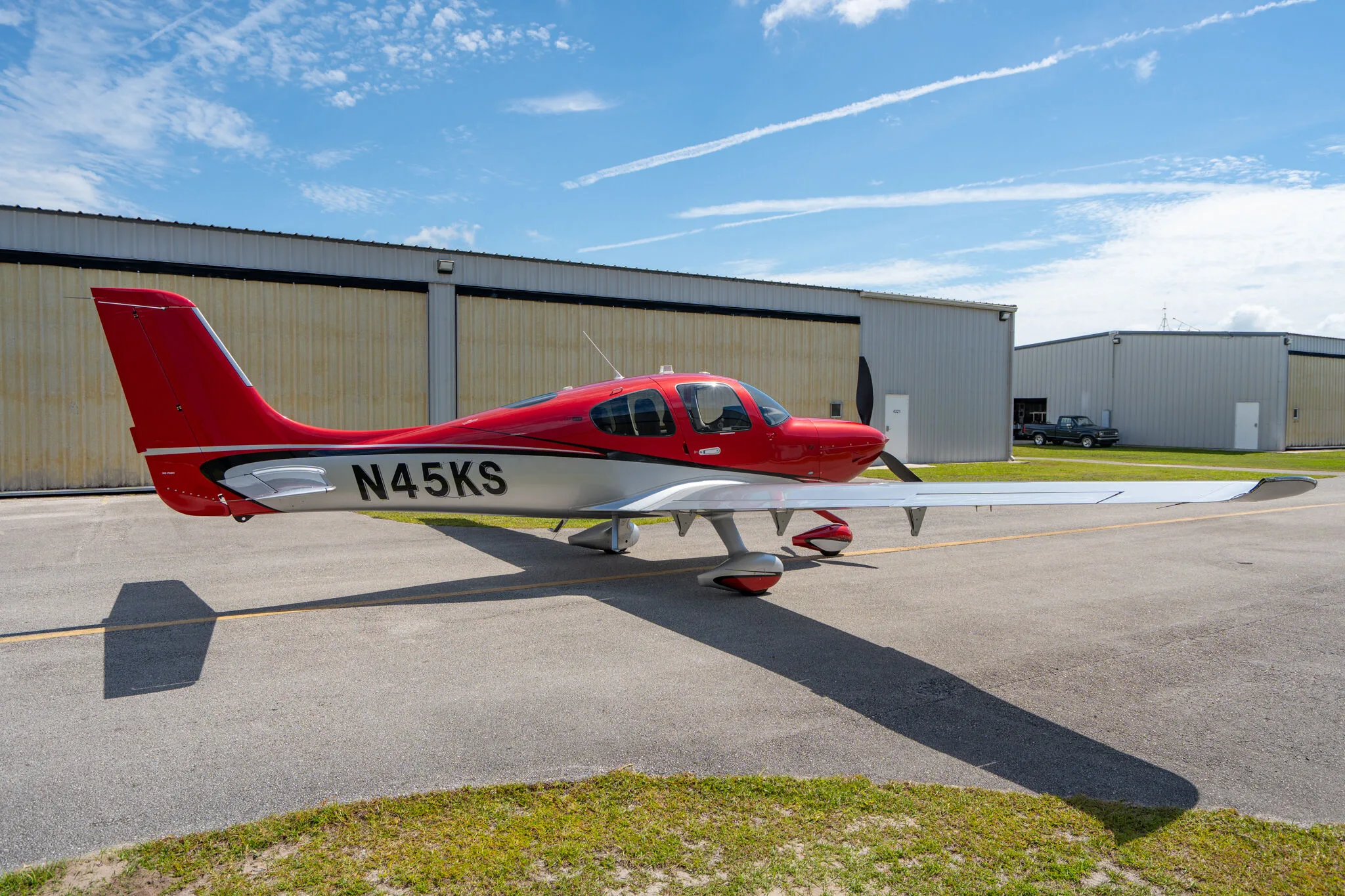 A red and silver Cirrus SR22 GTS (N45KS) parked on an airfield with hangars in the background.