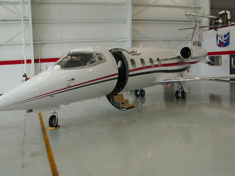 A white business jet with red and blue stripes, registration N518SB, parked inside a hangar with its main entry door open.