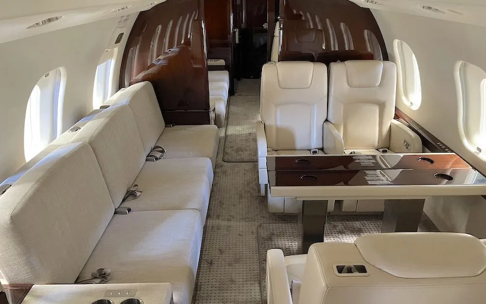 The spacious interior of a private jet featuring a cream sofa, individual seats, and a dining table.
