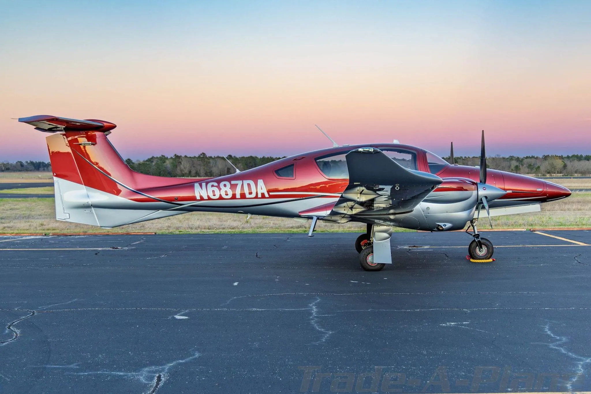 A side view of a red and silver Diamond DA62 aircraft parked on an airfield with sunset colors.