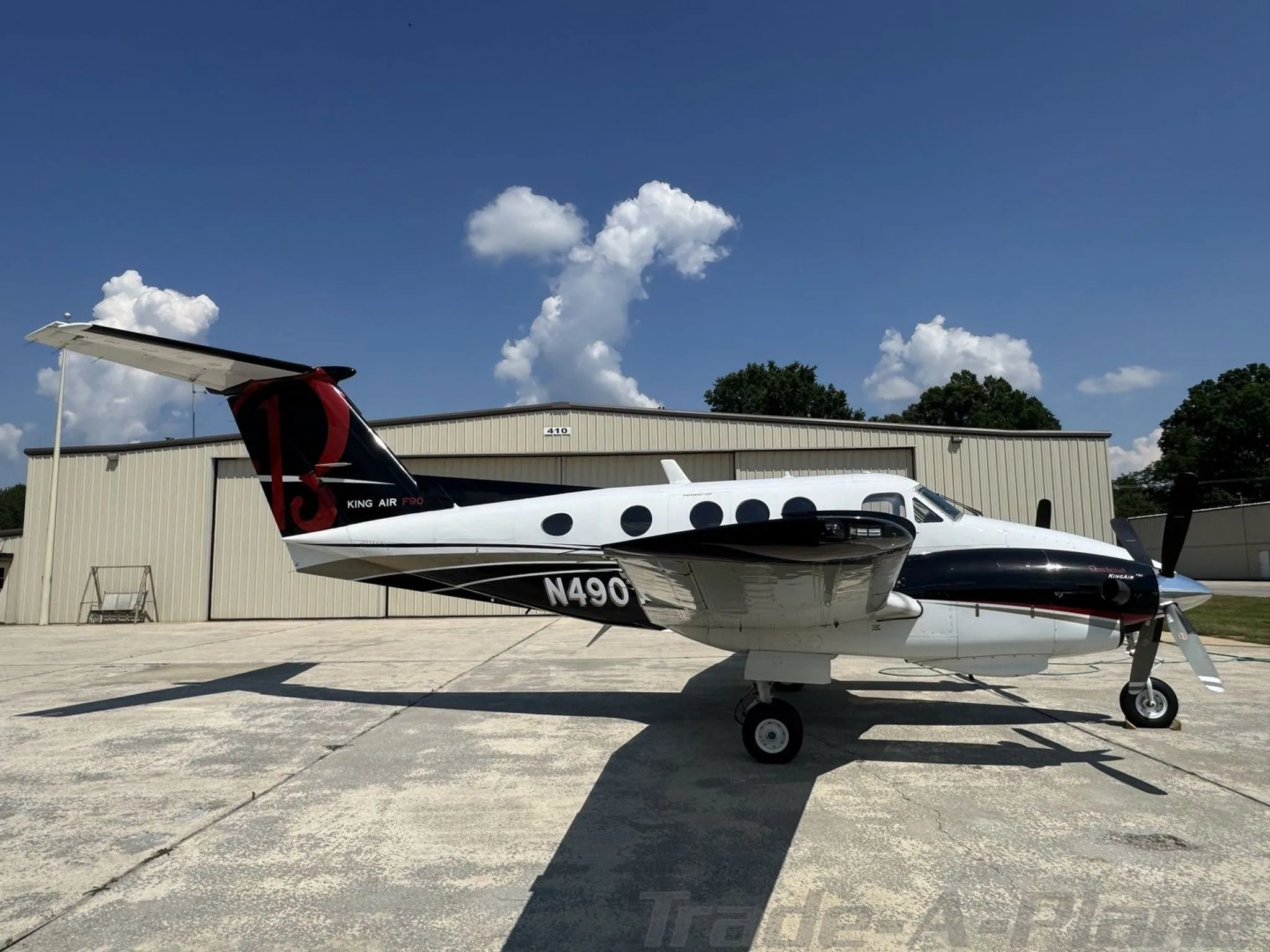 A side view of a white and black Beechcraft King Air F90, N490TX, parked in front of a hangar.