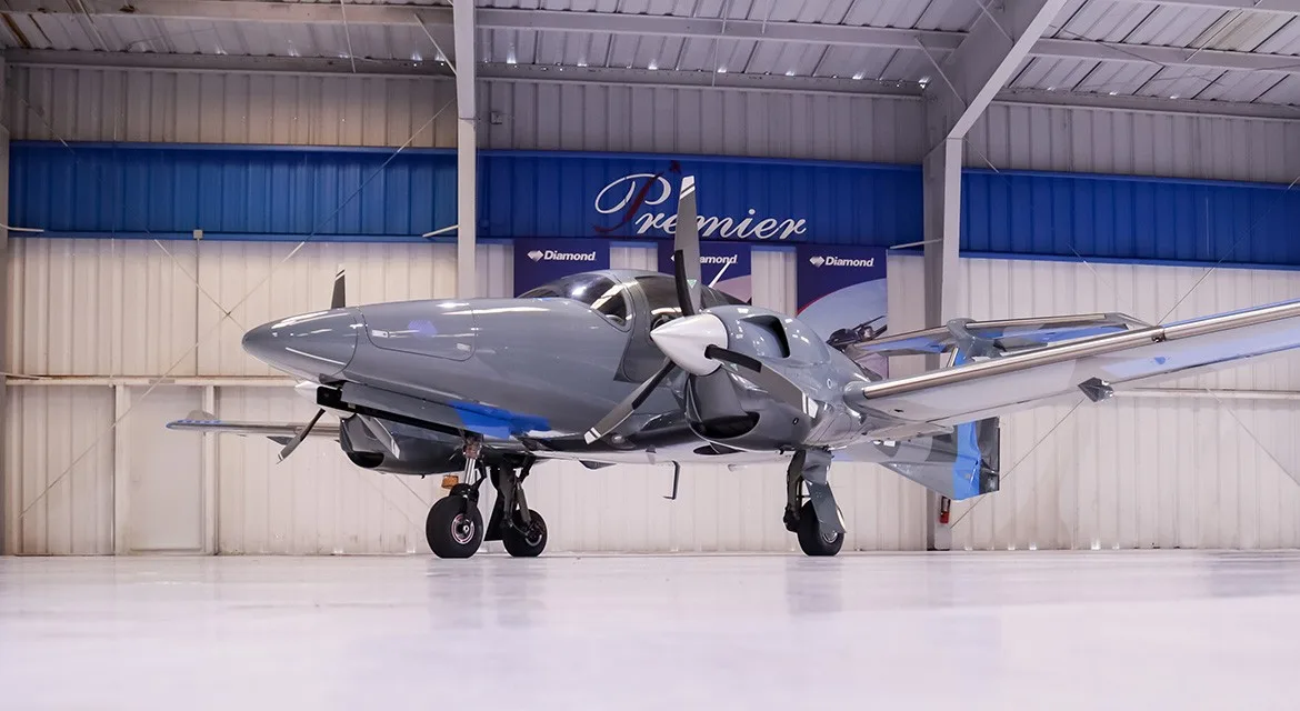 A low-angle front view of a gray and blue Diamond DA62 aircraft, registration N215E, in a hangar.