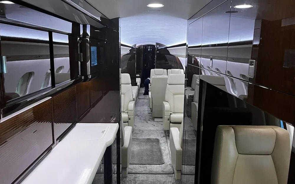 A view down the luxurious cabin of a private jet with light-colored seats and dark wood accents.