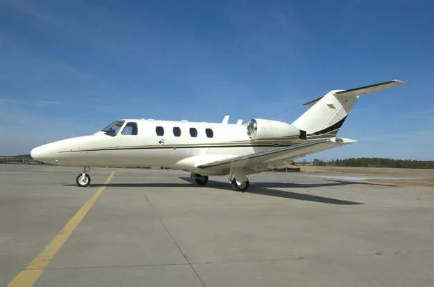 A white Cessna CitationJet aircraft with black and gold accents parked on an asphalt runway under a clear blue sky.